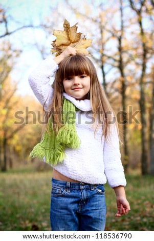 Beautiful little girl holding maple leaves and puts it in the head outdoors