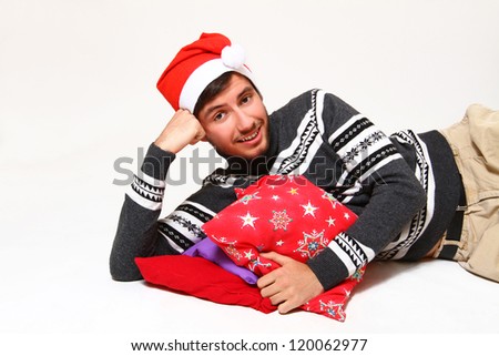 Smiling brunette guy  wearing Santa Claus hat lying with red pillows