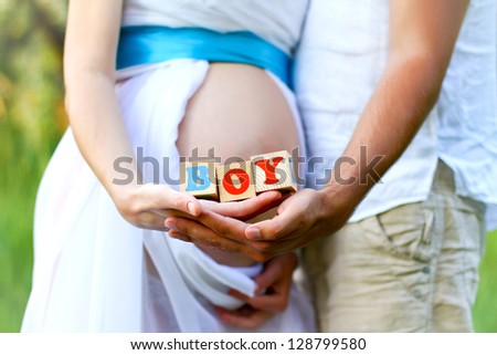 Close-up of the belly of a pregnant woman and of her husband holding boy cubes