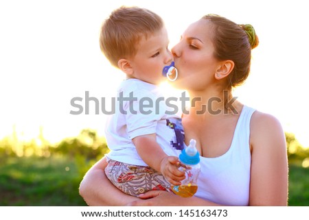 Mother kissing her son on  background of green trees