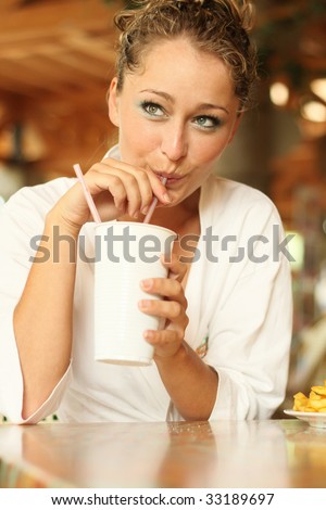young blond woman in bathrobe drinks with a straw out of a mug