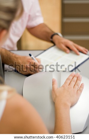 hand of a woman lies on a sensor device and a man notes some data