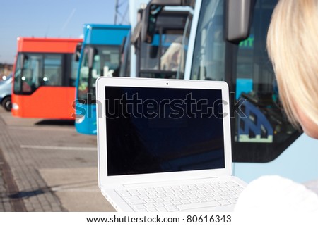 young blond woman with laptop in front of some busses/young blond woman stands with her laptop in front of a few busses