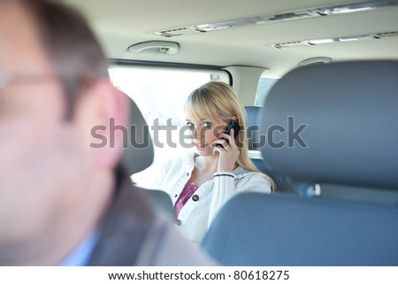 young blond woman with a smartphone on a backseat of a car/young blond woman with a smartphone on a backseat of a car