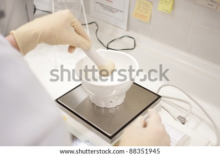 woman in a laboratory in a white smock with latex gloves, mortar and electronic balance/electronic balance