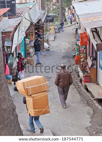 SHIMLA, INDIA - MARCH 19, 2014: Porter carrying a large load through one of the steep narrow streets of Shimla. This means of transporting goods is common in Indian towns and cities