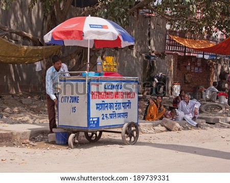 DELHI, INDIA - MARCH 28, 2014: A water seller plies his trade in the shade on a hot day. This type of trader is a common sight in Indian towns and cities, especially in summer months