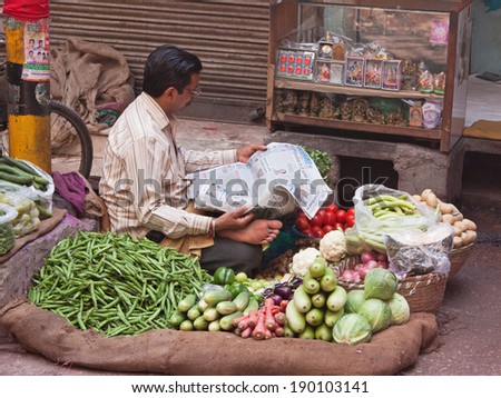 DELHI, INDIA - MARCH 22, 2014: Roadside vegetable seller catching up with the news in the Chandni Chowk bazaar in Shahjehanabad, Old Delhi