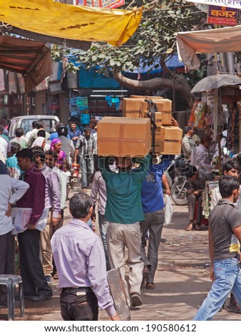 DELHI, INDIA - MARCH 28, 2014: A team of porters carry goods aloft through a bazaar in the heart of the city. The use of porters to transport goods in this way is common in Indian towns and cities