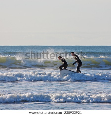 SAUNTON SANDS, ENGLAND - DECEMBER 3, 2014: Surfing couple riding the waves in unison. The bay in North Devon is popular with surfers and boarders