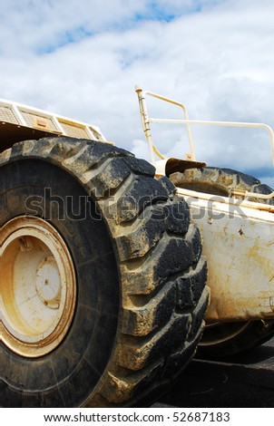 A big tractor, with big dirty wheels, with the blue and cloudy sky in the background.