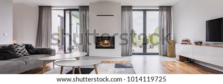 White, elegant living room with fireplace, tv, coffee table and couch, panorama