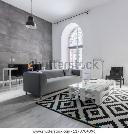 Loft apartment with gray sofa, pallet table, carpet and studio lamp