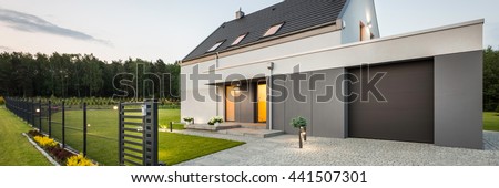 External view of stylish family house with fence, garage, stone driveway and garden, panorama
