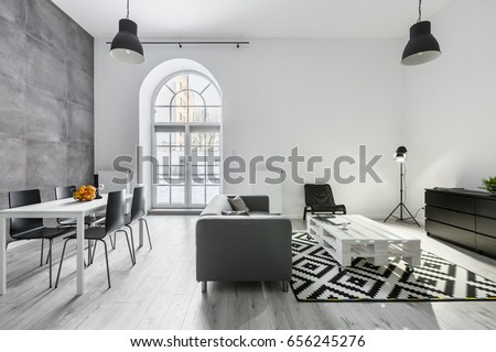 Modern loft interior with sofa, dining table with chairs, studio lamp and big window