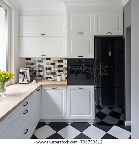 Small, white kitchen with modern chess flooring and black fridge