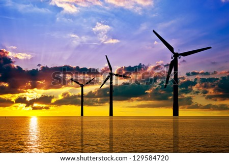 Silhouette of wind power stations over the sea at sunset.