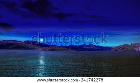 Night scene in mountain with full moon reflected in sea blue water.