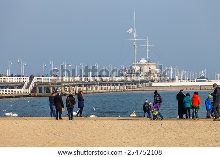 SOPOT, POLAND - FEBRUARY 14: Baltic coast scene of many people walk on beach, relaxing, feeding swans at the sea in Valentines Day and wooden pier in the distance, on February 14, 2015 in Sopot,Poland