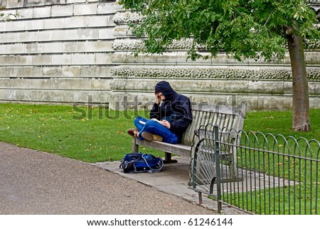 LONDON, ENGLAND - SEPTEMBER 15: Young male student sits on London park bench engrossed in study with open text books on September 15, 2010 in London, England