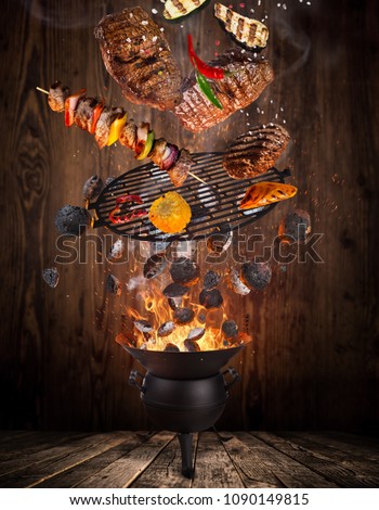Kettle grill with hot briquettes, cast iron grate and tasty meats flying in the air. Freeze motion barbecue concept.