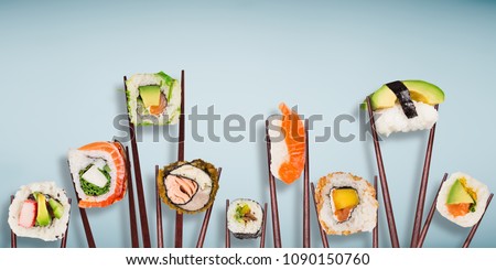 Traditional japanese sushi pieces placed between chopsticks, separated on light blue pastel background. Very high resolution image.