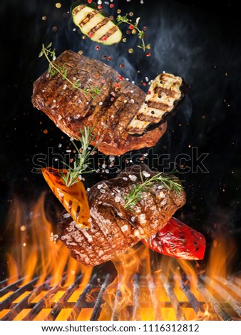Tasty beef steaks flying above cast iron grate with fire flames. Freeze motion barbecue concept.