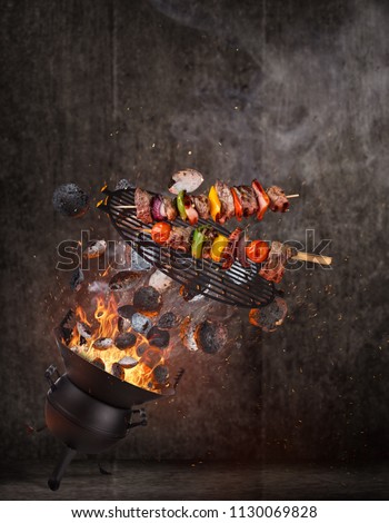 Kettle grill with hot briquettes, cast iron grate and tasty skewers flying in the air. Freeze motion barbecue concept.