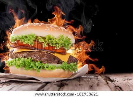 Delicious hamburger with fire flames on wooden background Delicious hamburger with fire flames on wooden background