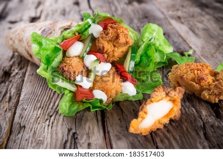 Chicken strips in a Tortilla Wrap with Lettuce on wood.