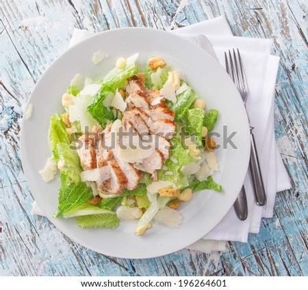 Caesar salad with chicken and greens on wooden table