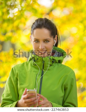 Young happy brunette woman listening to music in autumn park.