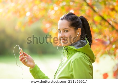 Young happy brunette woman listening to music in autumn park.