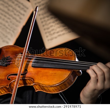 Young man with violin and flying notes on dark background