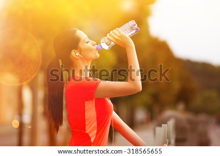 Brunette young woman runner drinking bottle of water.