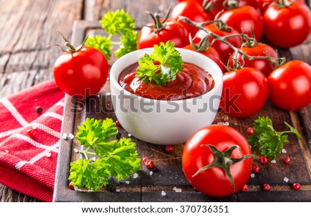 Bowl of tomato sauce and cherry tomatoes on wooden table, close-up.