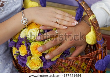 Hands of the groom and the bride on yellow purple wedding flowers