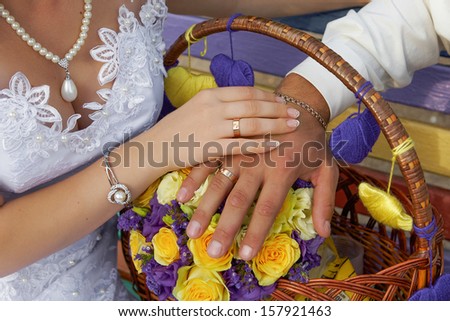 Hands of the groom and the bride on yellow purple wedding flowers