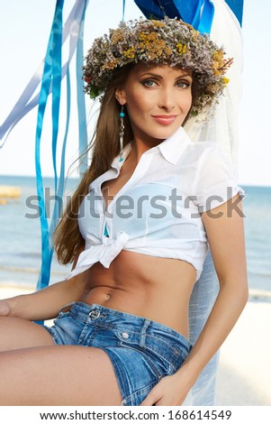 girl with a wreath and blue ribbons in shorts on a background of the sea