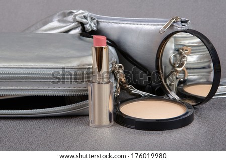Silver cases,  lipstick and powder on a gray background