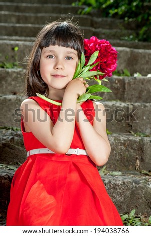 Charming little girl in a red dress sitting on stairs with peony