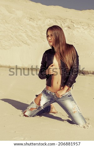 beautiful hot girl in ripped jeans and a leather jacket in the desert