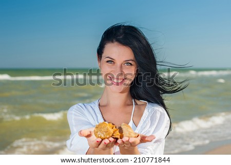 Young woman holing a shell in her hands on the seashore