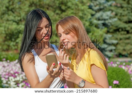 young Girls Applying Make up and Looking in the Mirror. Pretty Teens Having Fun and Putting Makeup Lipstick or Lip gloss. women Outdoors. Cosmetics