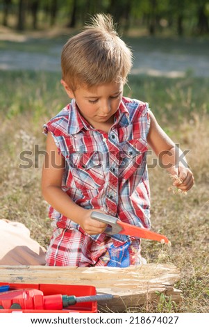 Little boy with toy hand tools drill and saw. Emotional, hard at work outside.