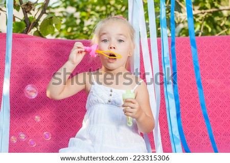 Happy little girl with soap bubbles on a pink background
