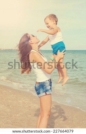 Happy family. Young mother throws up baby in the sky, on sunny day. Portrait mother and little son on the beach. Positive human emotions, feelings, emotions.
