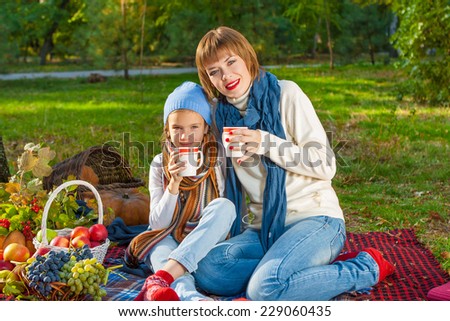 beautiful happy mother and daughter sitting on a picnic. With a cup of hot tea. Autumn harvest. Apples, pumpkins, grapes, viburnum.