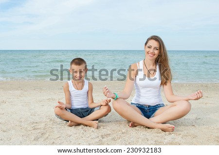 Happy family. Young happy beautiful  mother and her son doing yoga on coast of sea on beach.