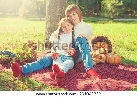 Beautiful mother and daughter sitting at a picnic on a sunny day. With apples. Autumn.